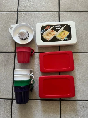 Plastmuggar, lunchlåda och citruspress - Säljer ett set med fyra stapelbara plastmuggar i rött, vitt, grönt och mörkblått, en vit citruspress samt en vit lunchlåda med två röda lock. Perfekt för picknick, utflykter eller köket. Allt är gjort i tålig plast och enkelt att rengöra.