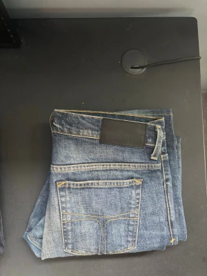 Blå raka jeans med kontrastsömmar från tiger of Sweden  - Säljer ett par klassiska blå jeans med raka ben och snygga kontrastsömmar från tiger of Sweden. Jeansen har fyra fickor och en svart patch bak i midjan. Materialet är slitstark denim i bomull och passformen är tidlös och enkel att matcha.