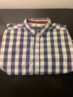 Blårutig skjorta från Gant - Klassisk blårutig skjorta från Gant med button-down krage och vita knappar. Skjortan har en bröstficka och är tillverkad i mjuk bomull. Perfekt för en stilren och avslappnad look.