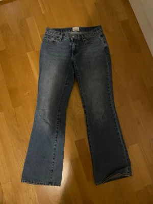 Blå bootcut jeans med låg midja - Säljer ett par klassiska blå bootcut jeans med låg midja och fem fickor. Jeansen har en lätt tvättad look och är tillverkade i denim. Perfekta för dig som gillar en avslappnad men ändå trendig stil.