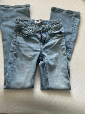Ljusblå bootcut jeans - Säljer ett par ljusblå bootcut jeans med klassisk femficksdesign och bälteshällor. Jeansen har en rak passform upptill och utsvängda ben. Tillverkade i mjukt denimtyg som ger en avslappnad look. Perfekta för dig som gillar retrostil och vill ha ett par bekväma jeans.