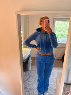  Juicy Couture velourset XS 💙 - Säljer ett par blå mjukisbyxor i velour med raka ben och dragsko i midjan. Byxorna har fickor framtill och matchar perfekt med en hoodie i samma material för en chill look. Supermjuka och sköna att ha på sig.