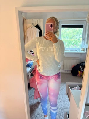 Galaxy-mönstrade aimn leggings i pastell - Säljer ett par leggings med galet snyggt galaxmönster i rosa, lila och blå toner. De har hög midja och vita detaljer vid vaden. Perfekta för dig som vill sticka ut på gymmet eller i vardagen. Materialet är stretchigt och följsamt för bästa komfort.