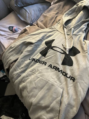  hoodie från Under Armour - Säljer en hoodie från Under Armour med stor svart logga och text på bröstet. Hoodien har huva med dragsko och en stor magficka framtill. Tillverkad i mjukt material som passar perfekt för chill eller träning.