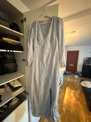 Ljusblå långklänning med broderi - Säljer en ljusblå långklänning med v-ringning och långa ärmar. Klänningen har fina broderade detaljer och en slits framtill. Perfekt för dig som gillar romantisk och stilren look. Använd en gång på midsommar för något år sedan 