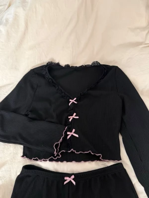 Svart pyjamas-set med rosa rosetter & volang - Säljer ett svart ribbat pyjamasset med långärmad topp och matchande byxor