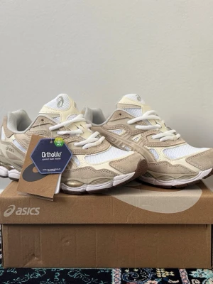 ASICS Gel-NYC Beige - Box & Receipt Included 🤍👟 - Sneakers i beige och vitt från Asics med meshpaneler och detaljer i mocka. Skorna har vita snören, Ortholite-innersula och en chunky sula som ger en sportig look. Perfekt för dig som gillar stilrena och bekväma sneakers.