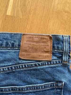 Levi's 502 blå jeans W33 L32 - Klassiska blå Levi's 502 jeans i rak modell. Jeansen har normalhög midja och är tillverkade i slitstark denim. Perfekta för en avslappnad och tidlös stil.