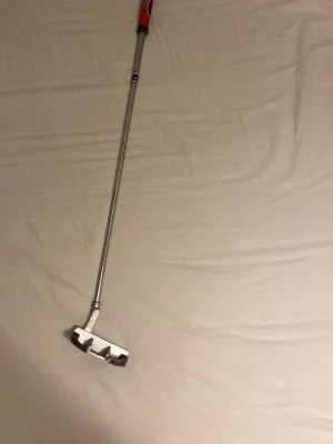 Spalding golfputter svart och silver - Golfputter från Spalding med svart och silverfärgat klubbhuvud och röd detalj på greppet. Klubbhuvudet har vita och röda markeringar för sikte. Perfekt för dig som vill förbättra ditt puttspel på greenen. Väldigt färsk och bra grepp nästan nytt.