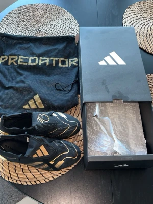 Adidas Predator Elite Belligold (Jude Bellingham) - Svart/guld limited edition med fold-over-tunga och JB-signatur. Kommer med originalpåse + box. Använda men i fint skick, normala slitagemärken på guldsulan.