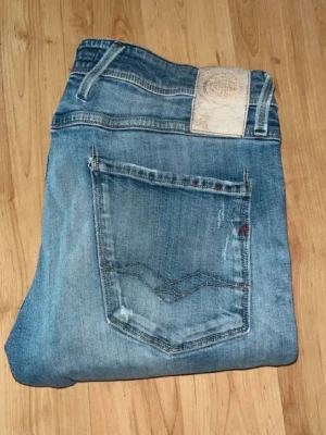 Replay Anbass jeans  - Ljusblåa Anbass jeans från Repaly med slitningar och hål på knäna. Midja 38cm, längd 115cm. JAG SKICKAR EJ FLER BILDER NÄR JAG BÄR JEANSEN! för bättre inblick i passformen rekommenderar jag att googla på modellnamnet. För storleksguide kolla måtten noggrant då jeansen alltid kan vara uppsydda heller krympta och jag ej tar emot returer :) (r13)