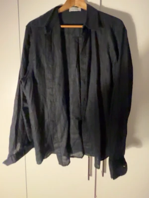 Blå linneskjorta  - Säljer en mörk blå skjorta i linne med klassisk krage och långa ärmar. Skjortan har en avslappnad passform och är perfekt för dig som gillar en enkel men stilren look. Passar till många olika outfits och är lätt att styla.