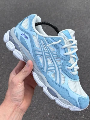  Nya Asics cream sky sneakers  - Snygga sneakers från Asics i ljusblått och vitt med meshpaneler och detaljer i mocka. Skorna har en chunky sula och klassisk snörning. Perfekta för dig som gillar sportig och trendig stil.