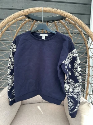 Sweatshirt strl. S - Mörkblå sweatshirt från Forever 21 med unika vita bandanamönstrade ärmar. Tröjan har rund halsringning och ribbade muddar vid ärmslut och nederkant.