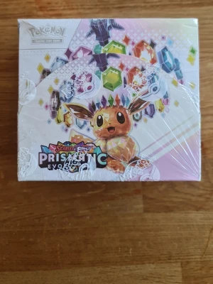 Pokémon Scarlet & Violet Prismatic - sealed - Pokémon Scarlet & Violet Prismatic Evolutions boosterbox med färgglad design och Eevee på framsidan. Boxen är dekorerad med prismatiska kristaller och har en vit och pastellfärgad bakgrund. Perfekt för samlare och Pokémon-fans.
