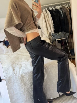 Svarta raka byxor i skinn - Säljer ett par svarta byxor i skinn med Bootcut/utsvängade passform och låg midja. De är köpta vintage och  i toppskick. Älskar! 