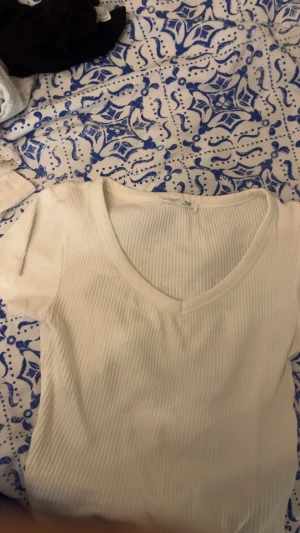 Vit ribbad topp från Primark - Säljer en enkel och stilren vit ribbad topp från Primark. Toppen har korta ärmar och v-ringad halsringning, vilket ger en clean och fräsch look. Perfekt att matcha med jeans eller kjol för en avslappnad stil.