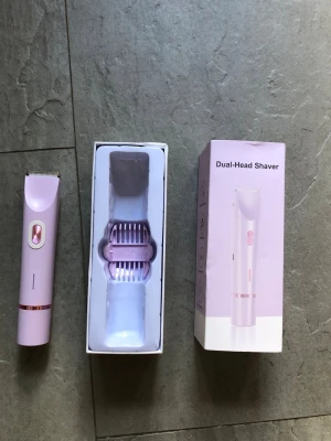 Ljuslila Dual-Head Shaver - Säljer en ljuslila elektrisk rakapparat med dubbla huvuden. Kommer med tillhörande huvuden och laddsladd i originalförpackning. Smidig design i plast med metallblad och lila detaljer. Perfekt för enkel och snabb hårborttagning. Kan användas i dusch.   Endast provad. 