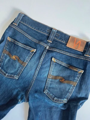 Nudie Jeans - Snygga blå jeans från nudie. Bortsett från hålet på bilden är de i mycket bra skcick. Om man orkar ta tag i det så erbjuder nudie gratis repetition på jeansen i deras butik. Så ganska lätt att fixa. Storlek W29 L32. Hör av dig vid frågor eller intresse!