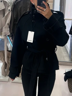 Svart trenchjacka från Bershka  - Stilren svart trenchjacka med hög krage, dubbelknäppning och bälte i midjan. Jackan har breda slag, axelklaffar och stora manschetter. Snygg och tidlös modell som passar till det mesta. Oanvänd, med prislapp kvar. Skriv för fler bilder🥰