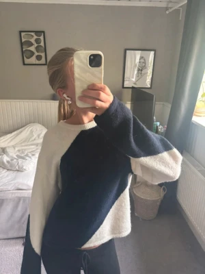 Mjuk stickad tröja i blått och vitt - Säljer en oversized stickad tröja med breda diagonala block i mörkblått och vitt. Tröjan har långa ärmar och en avslappnad passform, perfekt för dig som gillar en chill och trendig stil. Materialet känns fluffigt och mysigt.