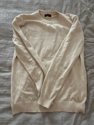 Beige stickad tröja  - En stilren beige stickad tröja med rund halsringning och ribbade muddar vid ärmslut och nederkant. Tröjan har en enkel och klassisk design som passar till det mesta. Perfekt för lager på lager och enkel att matcha med olika outfits.