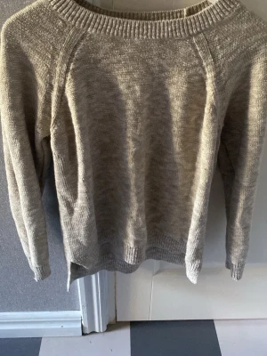 Beige stickad tröja med rund hals - En enkel och stilren beige stickad tröja med rund halsringning och långa ärmar. Tröjan har ribbstickade muddar vid ärmslut och nederkant, perfekt för lager-på-lager under kyliga dagar.