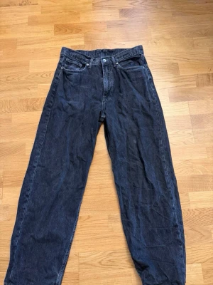 Svarta loose fit jeans med hög midja - Säljer ett par svarta loose fit jeans med hög midja och raka ben. Klassisk femficksmodell med knapp och dragkedja framtill. Jeansen är tillverkade i denim och har en avslappnad passform som ger en cool och trendig look.