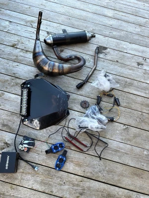 Mopeddelar och tillbehör mix (db 50 motor) - Säljer ett paket med olika mopeddelar, bland annat ett avgassystem från LeoVince, svart kåpa med LED-ljus, blinkers, drev, handtag i blått och svart samt diverse kablar och relä. Perfekt för dig som vill meka eller uppgradera din moppe. 