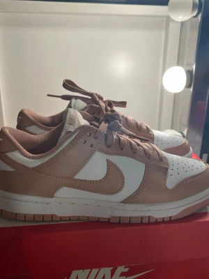 Nike Dunk Low Rose Whisper - Säljer ett par Nike Dunk Low sneakers i rosa och vitt. Skorna har klassisk låg siluett, perforerad tåbox och matchande rosa snörning. Kommer med original Nike-Box. Perfekta för en clean look.