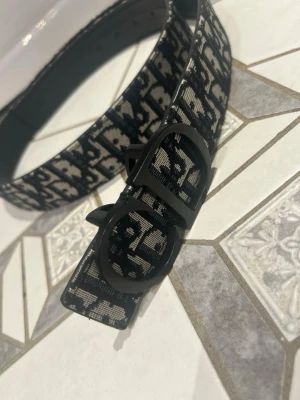 Svart och vit mönstrat bälte - Snyggt bälte med svart och vit mönstrad design och en stor, rundad spänne framtill. Bältet har ett trendigt mönster och känns riktigt stilrent. Perfekt för att lyfta vilken outfit som helst.