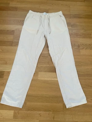 Beiga linnebyxor från Jack & Jones - Snygga och avslappnade beiga linnebyxor från Jack & Jones med dragsko i midjan och raka ben. Perfekta för en chill och stilren look. Byxorna har fickor på sidorna och är tillverkade i ett lätt och luftigt material.