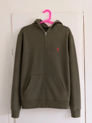 💚 Polo Ralph Lauren zip hoodie – M (10–12) - Klassisk zip-hoodie från Polo Ralph Lauren i snygg olivgrön/khakifärg. Hel dragkedja, huva, två fickor framtill och den ikoniska röda broderade ponnyloggan på bröstet. • Storlek: M (10–12 år) • Färg: Olivgrön/khaki • Hel dragkedja • Huva • Två fickor framtill • Röd broderad Polo-logga • Fint begagnat skick men har nån fläck! Tidlös modell och väldigt lätt att styla – perfekt för preppy/grisch/Stockholm-stil. Skriv gärna vid frågor eller om du vill ha mått!