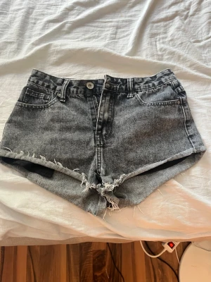 Grå denimshorts. - Snygga grå denimshorts med fransig, rå kant och klassisk femficksdesign. Shortsen har knapp och dragkedja framtill samt bälteshällor. Perfekta för en avslappnad stil under varma dagar.