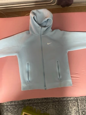 Babyblå Nike-nocta kofta - Nike NOCTA Zip Up – Babyblå  Nike NOCTA Zip Up i babyblå färg 💙 Använd flera gånger men fortfarande i bra skick. Finns ett pyttelitet hål vid mitten av dragkedjan, vilket syns på bilderna.  Säljer då jag inte använder den längre. 📦 Skickas snabbt och välpackad! 💬 Hör av dig vid frågor.
