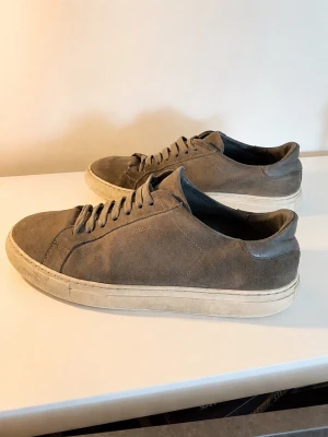 Grå mockasneakers med snörning - Snygga grå sneakers i mocka med klassisk låg profil och vita sulor. Skorna har snörning framtill och en stilren design som passar till det mesta. Perfekta för dig som gillar en clean och enkel look.