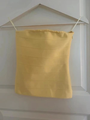 Gul bandeau tubtopp - Säljer en ljusgul bandeau tubtopp med smala axelband. Toppen har en enkel och clean design med diskreta horisontella sömmar. Perfekt för sommardagar och enkel att styla med olika outfits.