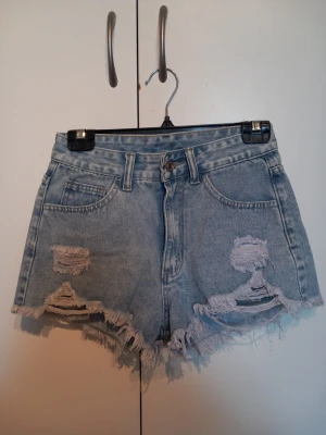 Ljusa blå jeansshorts - Säljer ett par ljusa blå jeansshorts med råa, fransiga kanter och slitna detaljer framtill. Shortsen har klassisk femficksdesign och medel midja. Perfekta för sommaren och ger en avslappnad, trendig look. De är köpte från Shein för 100 kr men aldrig använda för att de var för stora❤
