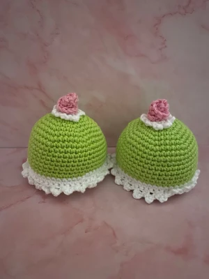 Virkade prinsessbakelser - Handgjorda virkade prinsessbakelser, i ljusgrönt garn med vit kant och rosa ros på toppen. Perfekt som dekoration eller till leksaksköket . Tillverkade i mjukt bomullsgarn och har en rund form med dekorativ spetskant.