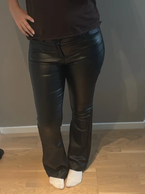 Svarta fuskskinnbyxor  - Snygga svarta byxor i fuskskinn med bootcut-modell. Byxorna har dragkedja och knapp framtill samt fickor bak. Använda 1 gång!