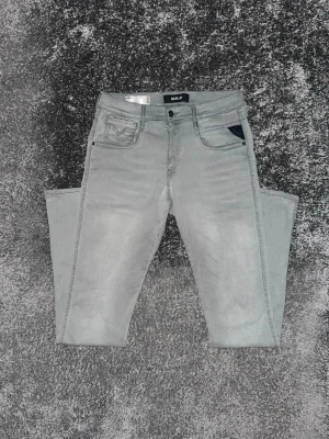 Gråa slim fit jeans från Replay - Snygga gråa slim fit jeans från Replay med klassisk femficksmodell och svarta detaljer på fickorna. Jeansen har en modern tvätt och raka ben, perfekta för en trendig och avslappnad stil. Materialet är mjukt och stretchigt för extra komfort.