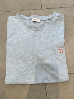 Ljusblå t-shirt från Les Deux - Snygg ljusblå t-shirt från Les Deux med diskret broderad logga i orange på bröstet. Klassisk rund hals och korta ärmar. Pefekt skick!!