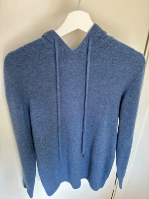 Blå cashmere hoodie  - Säljer en stilren blå cashmere hoodie med huva och dragsnören.Långärmad modell med ribbade muddar vid ärmslut och nederkant. Perfekt för dig som gillar en enkel men snygg look.