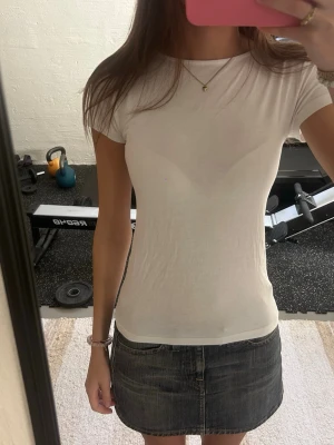 Vit tight t-shirt med öppen rygg - Säljer en enkel och stilren vit t-shirt med tight passform och korta ärmar. T-shirten har en snygg detalj med öppen rygg som ger en extra touch. Perfekt att matcha med jeans eller kjol för en clean look.