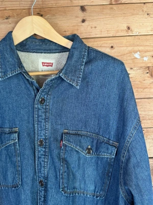 Levi’s fodrad jeansskjorta denim overshirt XL - Levi’s denim overshirt med sherpa XL  Levi’s denimskjorta/overshirt i mellanblå denim med sherpafodrad kropp, stora bröstfickor och klassisk röd Levi’s-tab. Rejäl och avslappnad passform som fungerar mer som en lätt jacka än skjorta. Snygg naturlig fading och tydlig workwear-känsla.  XL Regular | Bröst 61 cm | Axlar 55 cm | Ärm 62 cm | Längd 81 cm  #levis #denim #workwear #sherpa