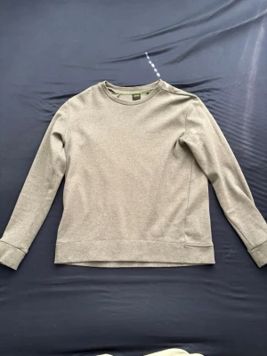 Boos hoddie grå - En stilren beige sweatshirt med rund halsringning och långa ärmar. Tröjan har en enkel design utan tryck eller mönster och breda muddar vid ärmslut och nederkant. Perfekt för en avslappnad look.
