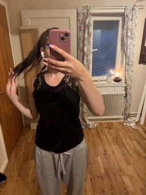 Svart linnetopp med spetsdetaljer - Snygg svart linnetopp med spets vid axlarna och rund halsringning. Toppen är ärmlös och har en feminin touch tack vare de fina spetsdetaljerna. Perfekt att styla med jeans eller kjol för en trendig look.