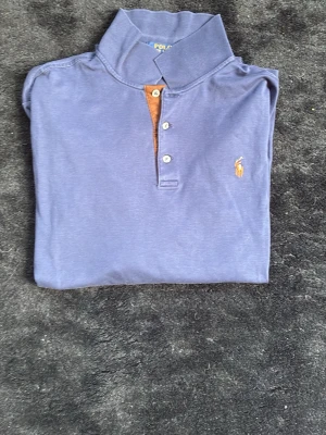Blå långärmad henley från Polo Ralph slim fit Lauren - Snygg blå långärmad henley från Polo Ralph Lauren med klassisk krage och tre knappar framtill. Ikoniska broderade loggan i gult på bröstet. Tillverkad i mjuk bomull, perfekt för en avslappnad men stilren look. Slim fit
