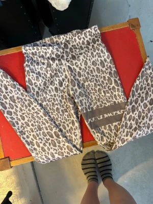 Leopardmönstrade tights från Stronger - Snygga tights från Stronger i leopardmönster med beige och bruna toner. Hög midja och två gråa ränder på ena benet. Tillverkade av 85% återvunnen polyester och 15% elastan för skön stretch och passform. Använd fåtal gånger