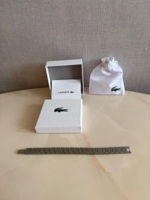 Lacoste armband🐊 - Vinted-beskrivning  Oanvänt Lacoste-armband i nyskick 🐊✨ Aldrig använt. Armbandet är ca 20 cm men storleken kan enkelt justeras så att det passar perfekt. Stilrent och exklusivt – passar både till vardags och fest 💎🔥 Perfekt som present 🎁